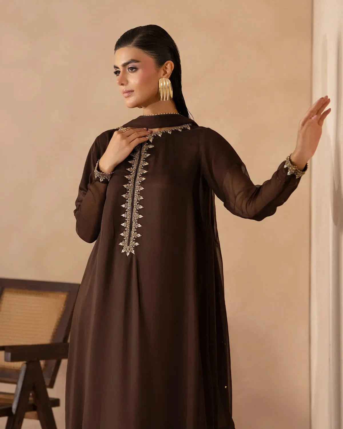A woman modeling a dark brown long-sleeve kurta with ornate silver embroidery around the neckline and down the center front, posed against a warm beige wall.