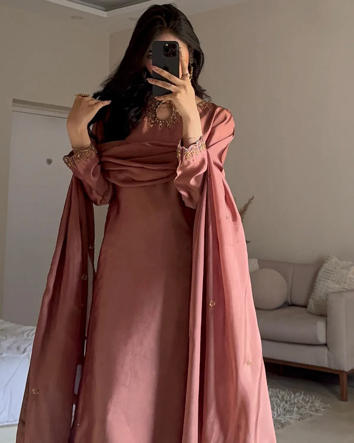 A woman takes a mirror selfie wearing a dusty rose pink traditional dress with a matching draped shawl featuring gold embroidery on the cuffs and neckline.