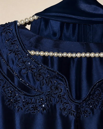 Close-up of a navy blue satin garment with floral embroidery and beadwork, decorated with a pearl beaded trim across the neckline.