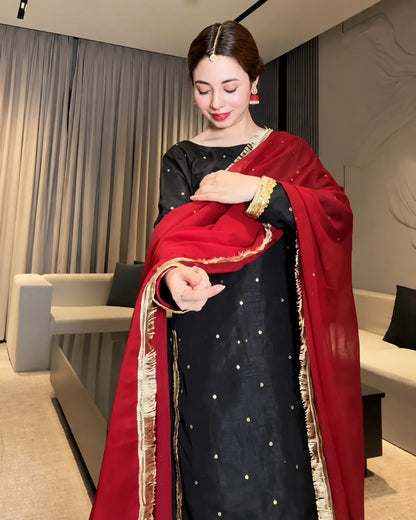 A woman models a traditional Indian outfit consisting of a black salwar with gold dot embroidery, paired with a deep red dupatta featuring gold zari borders.