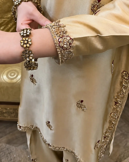 Close-up of a person wearing an ornate cream-colored traditional outfit with gold embroidery and embellished wrist bracelets.