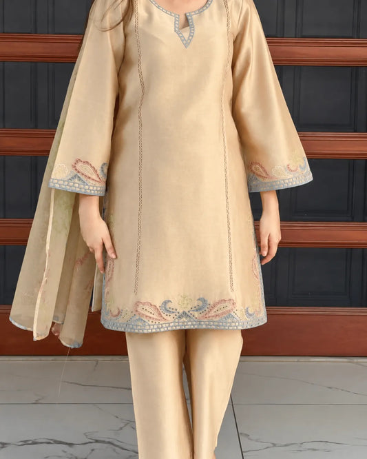 A model wearing a beige three-piece traditional South Asian outfit, featuring a straight kurta with blue and pink embroidered borders, matching trousers, and a coordinating dupatta, set against a dark paneled background.