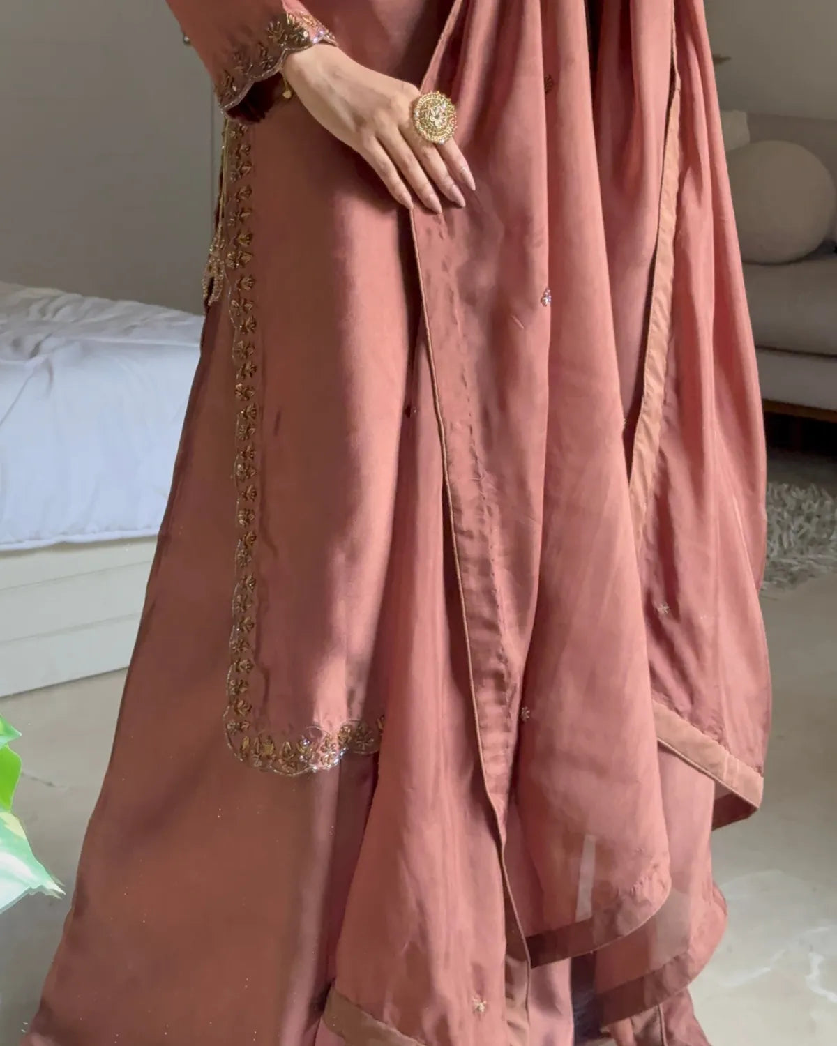 A close-up of a dusty rose pink traditional dress with gold embroidery, worn by a model in an indoor setting.