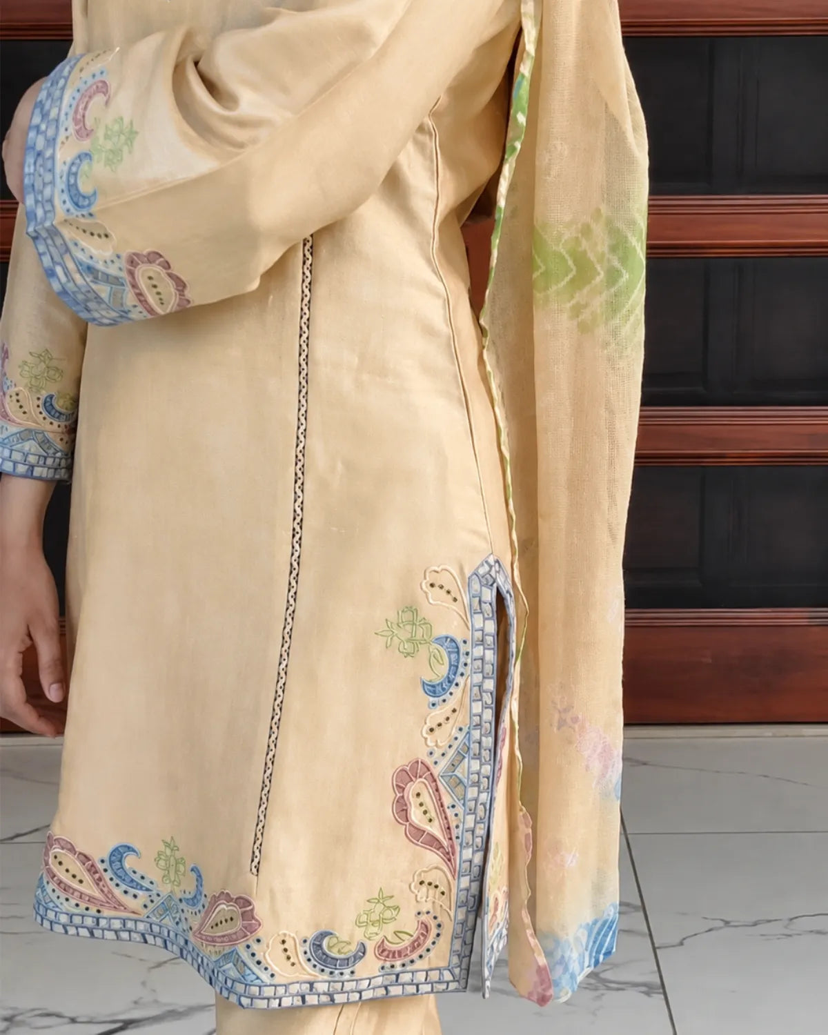 A close-up of a beige traditional outfit with colorful paisley embroidery in blue, green, and pink, featuring a matching dupatta draped over the shoulder.