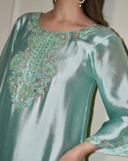 A close-up of a woman wearing a mint green satin kurta with intricate multicolor embroidery around the neckline and sleeve cuffs.