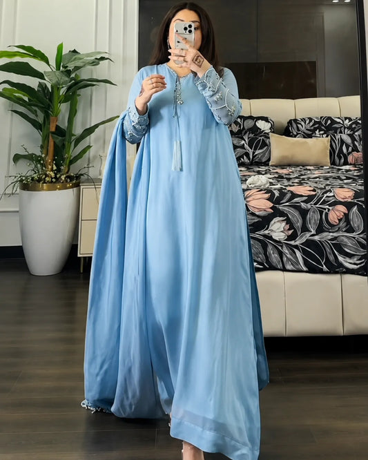 A woman takes a mirror selfie in a bedroom wearing a light blue traditional long dress with lace sleeves and a matching sheer draped overlay.