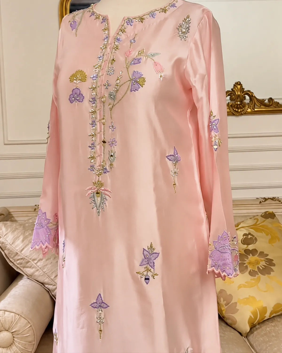 A light pink satin long kurta with intricate floral and butterfly embroidery in purple, gold, and green, displayed on a mannequin in an elegant indoor setting.