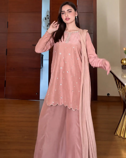 A woman modeling a dusty pink traditional South Asian outfit with a matching dupatta, featuring a long kurta with silver mirror work embroidery and wide-leg trousers, set against an indoor background with wooden flooring and doors.