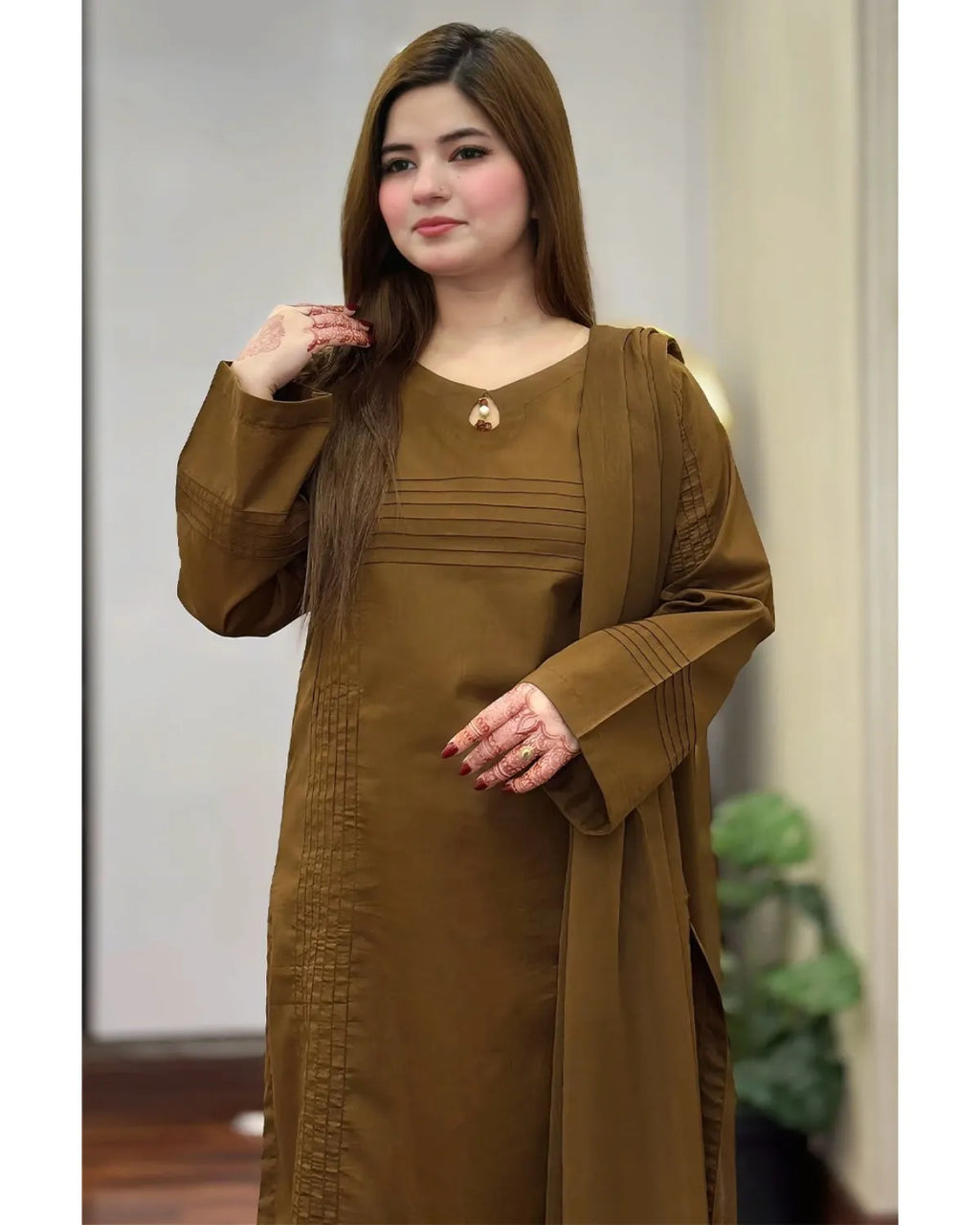 A woman wearing a long-sleeved brown modest dress with a matching draped shawl, standing in an indoor setting.
