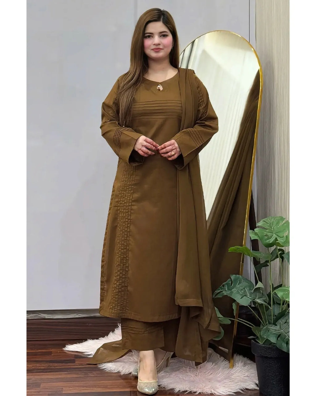 A woman modeling a brown long kurta set with matching pants and a draped dupatta, standing in front of a large arched mirror in an indoor setting.