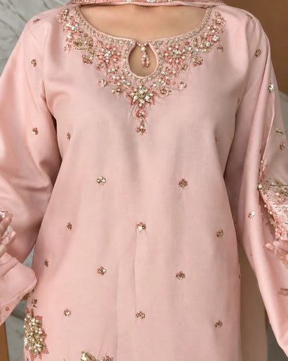 A light pink traditional long-sleeve tunic with ornate floral embroidery and beadwork around the neckline, decorated with scattered small metallic embellishments, shown on a model.