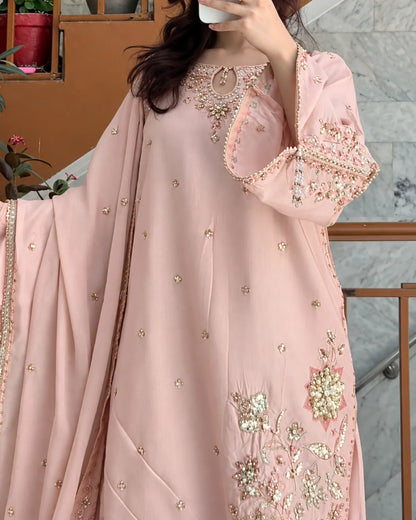A woman wearing a light pink traditional outfit with intricate gold and silver embroidery, featuring a long kurta with wide sleeves and a matching dupatta, photographed in an indoor setting.