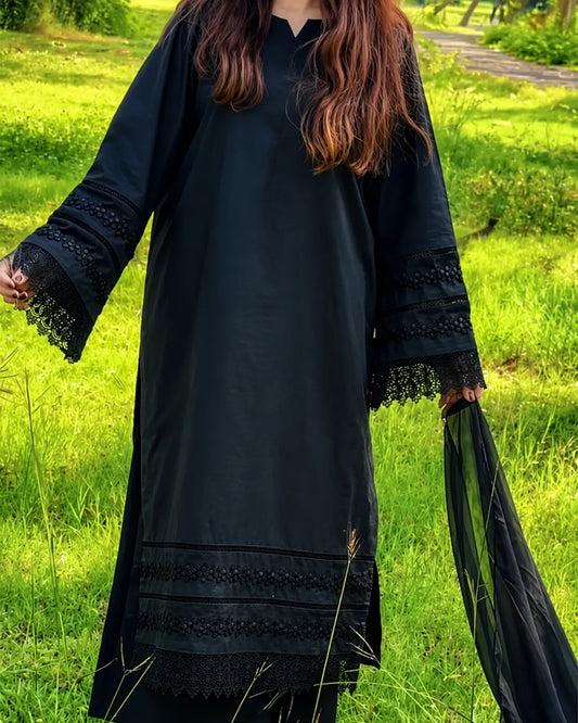 A woman wearing a long black tunic dress with lace trim on the sleeves and hem, standing outdoors in a grassy field.
