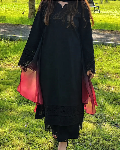 A woman wearing a black long-sleeve tunic dress with sheer red gradient side panels and black lace trim, standing outdoors on a grassy lawn.