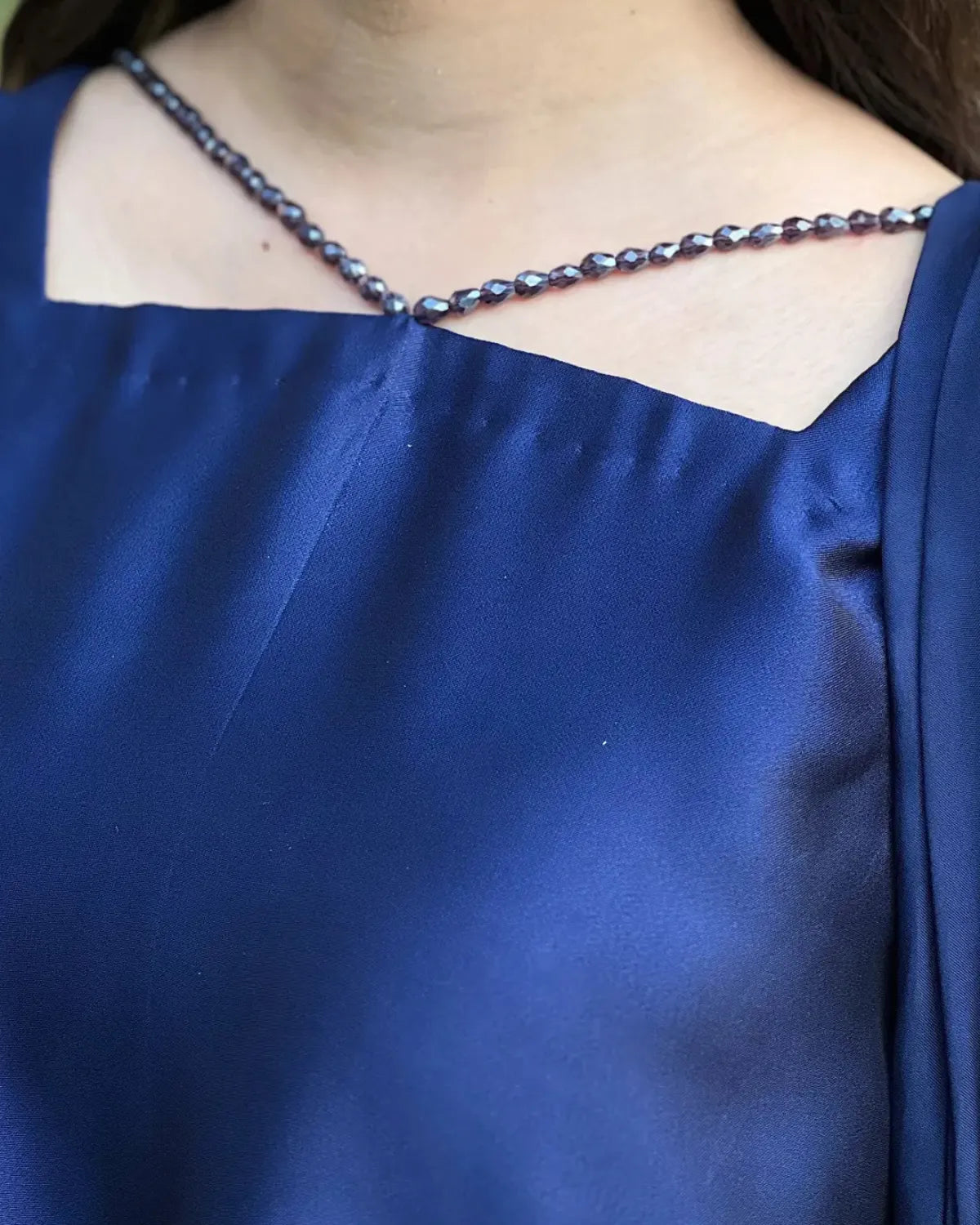 A close-up of a person wearing a royal blue satin dress with a beaded neckline featuring small dark purple beads.